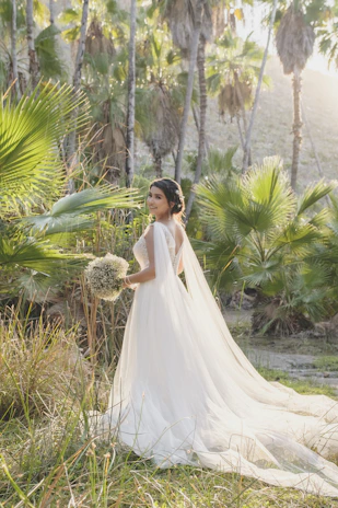 An elegant bride walking through a garden of white and mauve flowers, sunlight filtering softly.
