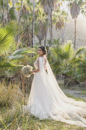 An elegant bride holding a bouquet of white and blush roses in a sunlit garden