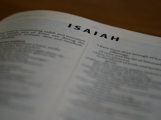 A close-up view of an open book with the title 'ISAIAH' prominently displayed at the top of the page. The text below is slightly blurred, focusing attention on the chapter title.