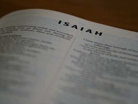 A close-up view of an open book with the title 'ISAIAH' prominently displayed at the top of the page. The text below is slightly blurred, focusing attention on the chapter title.