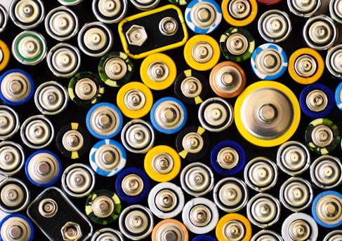 An assortment of batteries of various sizes and shapes. The arrangement is tight and close-up, showing the tops of the batteries with different colored labels.