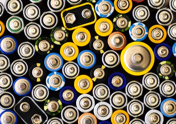 An assortment of batteries of various sizes and shapes. The arrangement is tight and close-up, showing the tops of the batteries with different colored labels.