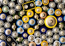 An assortment of batteries of various sizes and shapes. The arrangement is tight and close-up, showing the tops of the batteries with different colored labels.