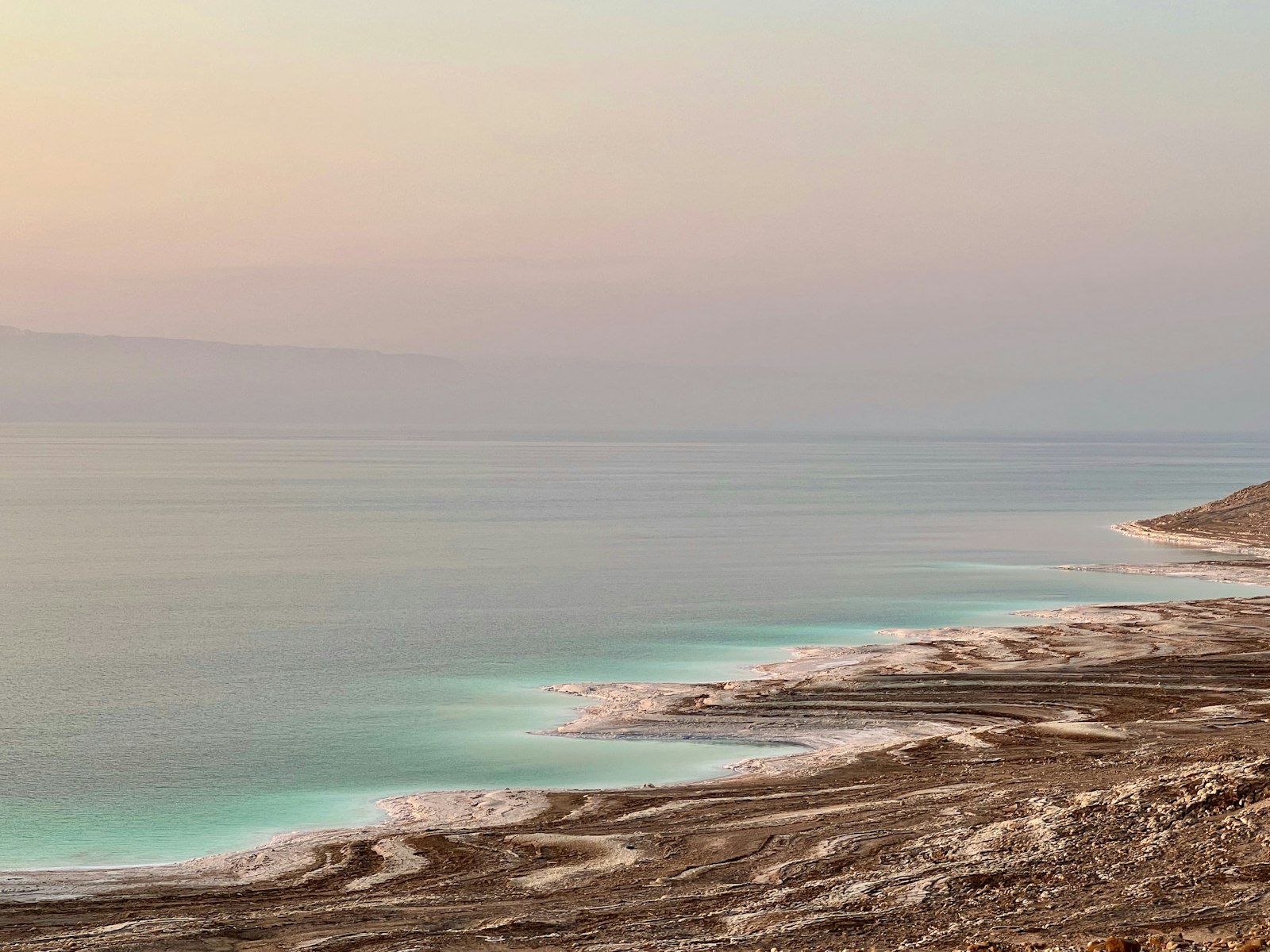 The salt-fringed shoreline of the Dead Sea glowing in soft sunset light