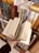A hand holding an open book with visible text, surrounded by neatly arranged shelves filled with various books. The books have colorful spines with text, indicating a library or bookstore setting.