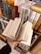 A hand holding an open book with visible text, surrounded by neatly arranged shelves filled with various books. The books have colorful spines with text, indicating a library or bookstore setting.