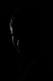 The image features a silhouette of a person's face with minimal lighting, creating a mysterious and dramatic effect. The focus is on the contours and shadows, giving a stark contrast against the dark background.