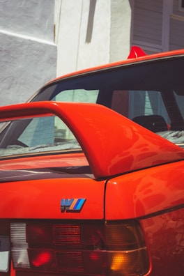 Close-up of a vibrant red spoiler mounted on a white coupe, showcasing its aerodynamic curves.