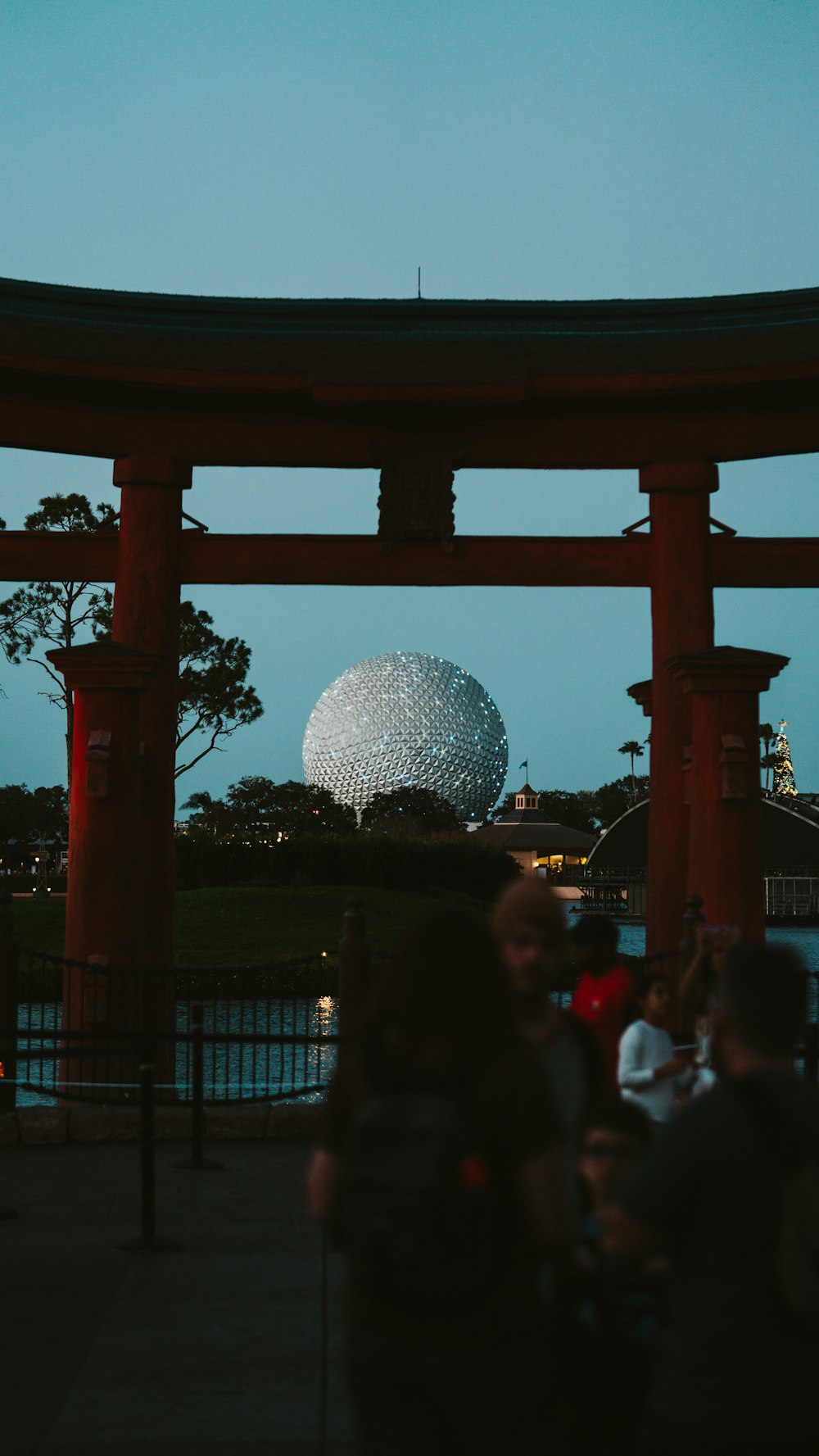 a group of people standing under a structure with a sphere in the background