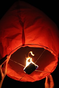 Close-up of hands gently holding a glowing red sky-themed lantern.