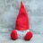 A fabric gnome dressed in a miniature sports jersey, holding a tiny ball, sitting on a wooden shelf.