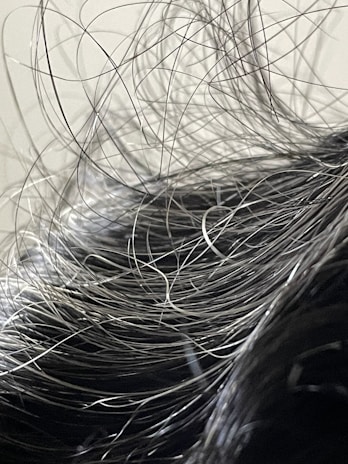 A close-up view of hair with numerous loose strands intertwined and overlapping. The strands appear to be gray or silver, indicating natural or dye-induced color. The background is blurred and neutral, focusing attention on the texture and flow of the hair.