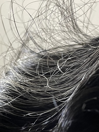A close-up view of hair with numerous loose strands intertwined and overlapping. The strands appear to be gray or silver, indicating natural or dye-induced color. The background is blurred and neutral, focusing attention on the texture and flow of the hair.