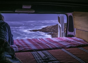 A comfortable van with open doors showing cozy interior seats, parked near a coastal road
