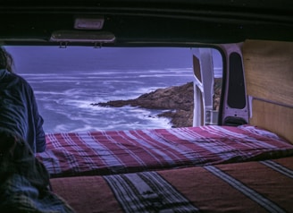 A comfortable van with open doors showing cozy interior seats, parked near a coastal road