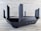 A sleek, black router with multiple angular antennas extending upwards and outwards on a wooden surface. The router has a modern design, featuring vents for airflow and buttons on the front panel. The background is a neutral, textured wall.