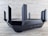 A sleek, black router with multiple angular antennas extending upwards and outwards on a wooden surface. The router has a modern design, featuring vents for airflow and buttons on the front panel. The background is a neutral, textured wall.