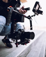 A camera setup attached to a stabilizer is being held. The equipment includes a camera with a large lens and various attachments, likely used for filming.