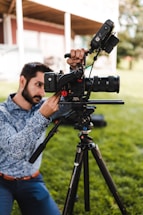 A photographer adjusting a camera on a tripod outdoors.