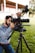 A professional photographer adjusting a high-end camera on a tripod outdoors.