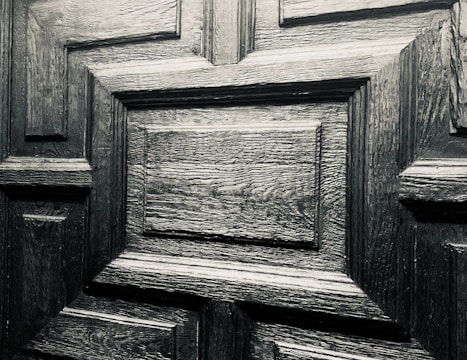 A detailed close-up of a wooden door with a geometric pattern. The wood appears to be dark and polished, showcasing its distinct grain and texture.
