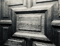 A detailed close-up of a wooden door with a geometric pattern. The wood appears to be dark and polished, showcasing its distinct grain and texture.
