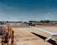 A small private jet is positioned on an airport tarmac with a clear blue sky in the background. The aircraft appears to be undergoing maintenance or preparation, as a red tow vehicle is attached to it at the front. Surrounding the plane are various airport vehicles and equipment. The scene includes a wide expanse of the runway and grassy areas in the distance.