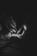 A black and white photograph captures a close-up of a person's hands wearing gloves, holding a surgical instrument over a surface, possibly during a medical procedure.