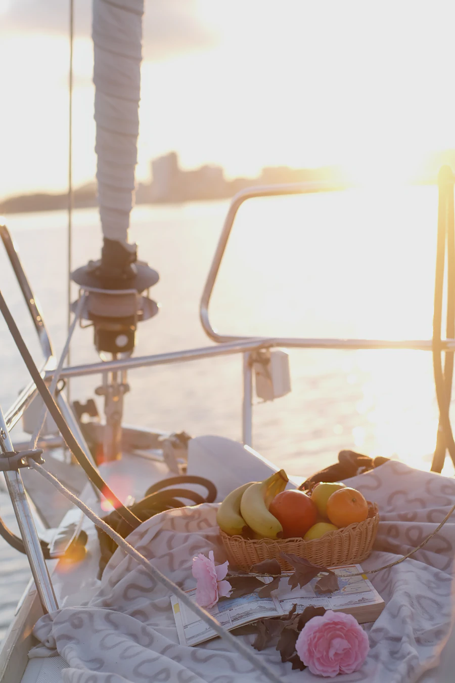 Mesa servida con frutas y rosas sobre la cubierta de un velero, bañada por la luz del atardecer