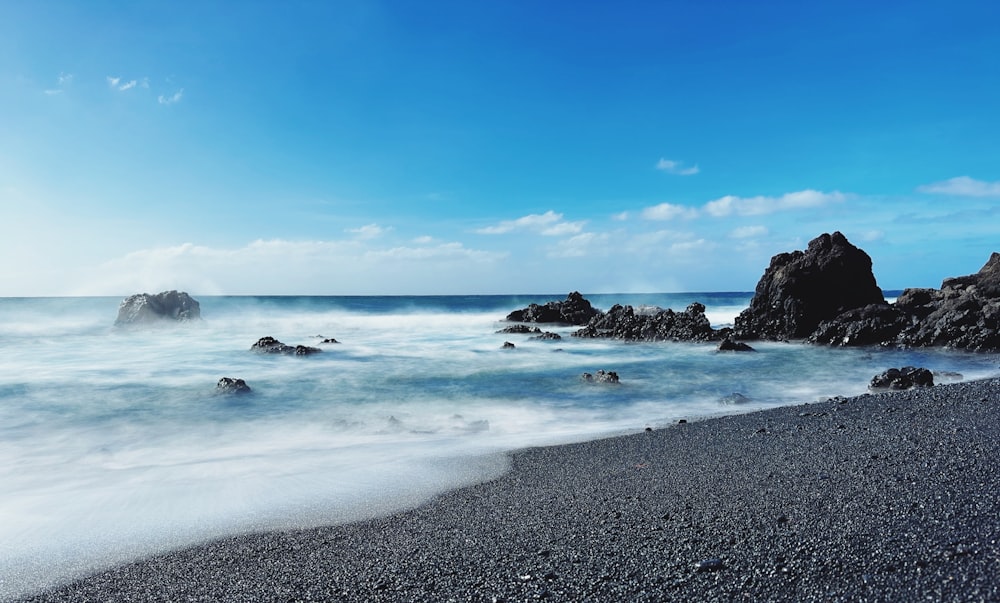 a rocky beach with a body of water and a blue sky