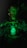 A person with shimmering green makeup and elaborate jewelry holds a bottle labeled 'Sexto Abrismo'. The scene is dimly lit with a green hue, giving it a mystical and otherworldly appearance.