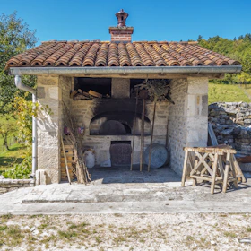 A rustic stone oven glowing with fiery embers, ready for outdoor cooking on a concrete terrace.