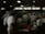 A busy commercial kitchen with several chefs in white uniforms and hats working diligently. The chefs appear to be preparing food amidst various cooking utensils and large pots. The environment is dimly lit with a focus on functionality.