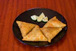 Close-up of golden, crispy samosas with chutney on the side.