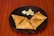 Three crispy golden-brown samosas are placed on a black round plate with a few wedges of lime. The plate is set against a rich wooden surface.