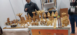 Finished wooden sculptures displayed on rustic tables surrounded by festival visitors.