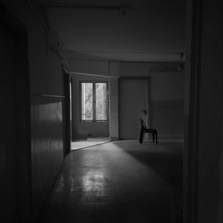 A shadowy room with a single chair under a harsh spotlight, evoking suspense