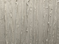 A textured surface featuring vertical streaks and ridges, likely created using plaster or a similar material. The pattern is irregular, with some areas appearing more pronounced than others.