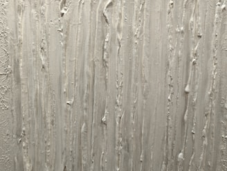 A textured surface featuring vertical streaks and ridges, likely created using plaster or a similar material. The pattern is irregular, with some areas appearing more pronounced than others.