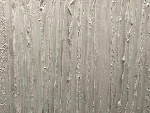A textured surface featuring vertical streaks and ridges, likely created using plaster or a similar material. The pattern is irregular, with some areas appearing more pronounced than others.