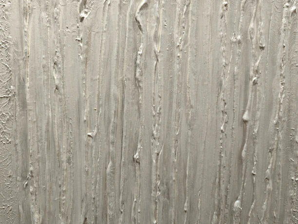 A textured surface featuring vertical streaks and ridges, likely created using plaster or a similar material. The pattern is irregular, with some areas appearing more pronounced than others.