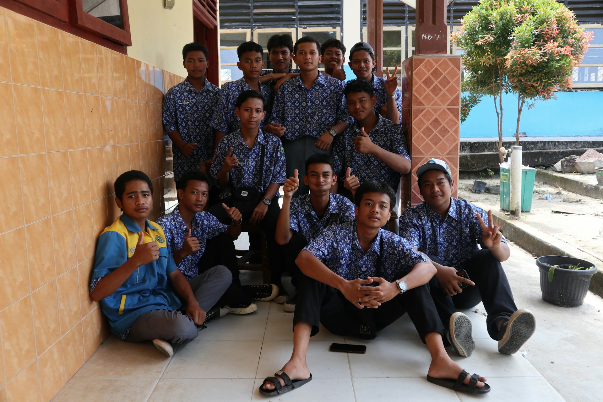 Youth volunteers planting trees together in a sunny community park, wearing matching blue and orange Astara Youth Hub t-shirts.