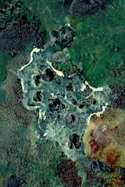 An abstract, textured landscape with swirling patterns of green, blue, and earth tones. The image features a mix of darker and lighter areas, creating a sense of depth and complexity.