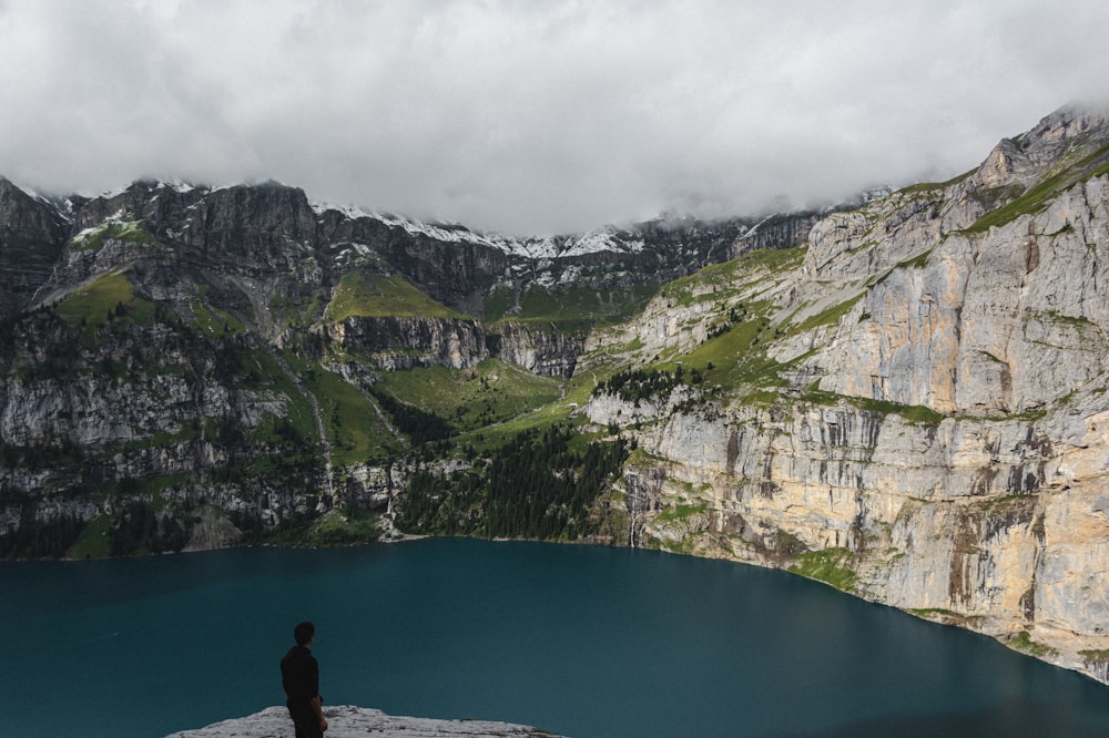 Una persona in piedi su una scogliera sopra l'acqua con le montagne sullo sfondo
