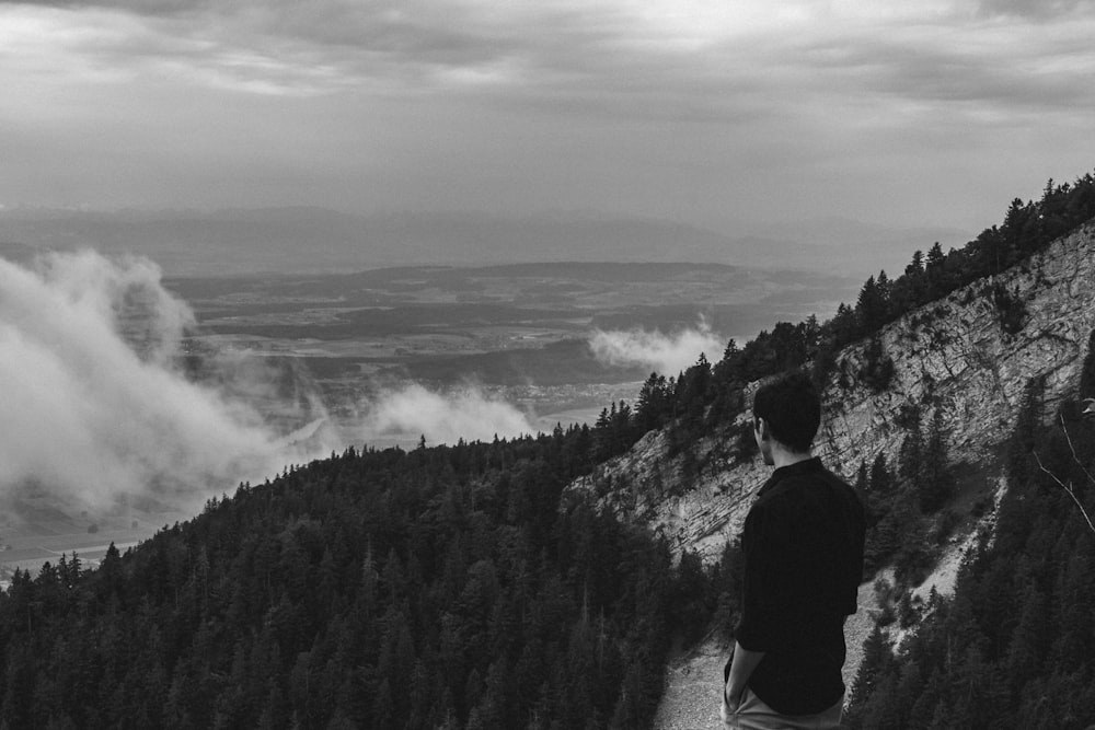 a man standing on a cliff overlooking a valley with clouds