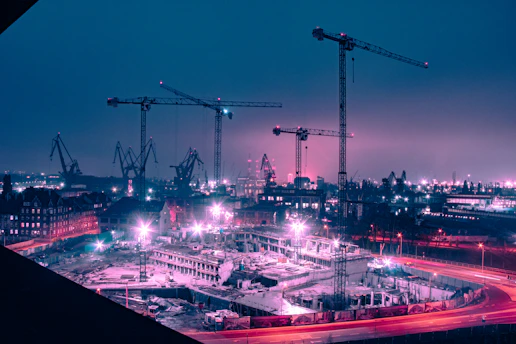 A vibrant green fluorescent-lit construction site at dusk showcasing heavy machinery and workers in action.
