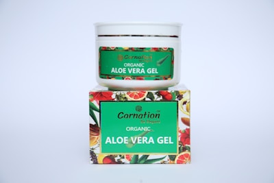 A white container with a green label for 'Carnation Organic Aloe Vera Gel' is placed on top of a colorful box featuring images of various fruits and flowers.