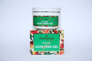 A white container with a green label for 'Carnation Organic Aloe Vera Gel' is placed on top of a colorful box featuring images of various fruits and flowers.