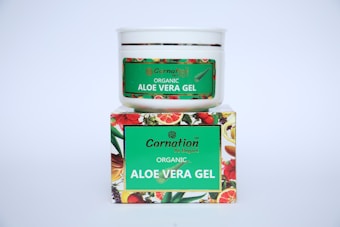 A white container with a green label for 'Carnation Organic Aloe Vera Gel' is placed on top of a colorful box featuring images of various fruits and flowers.