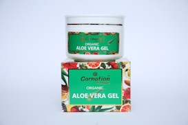 A white container with a green label for 'Carnation Organic Aloe Vera Gel' is placed on top of a colorful box featuring images of various fruits and flowers.